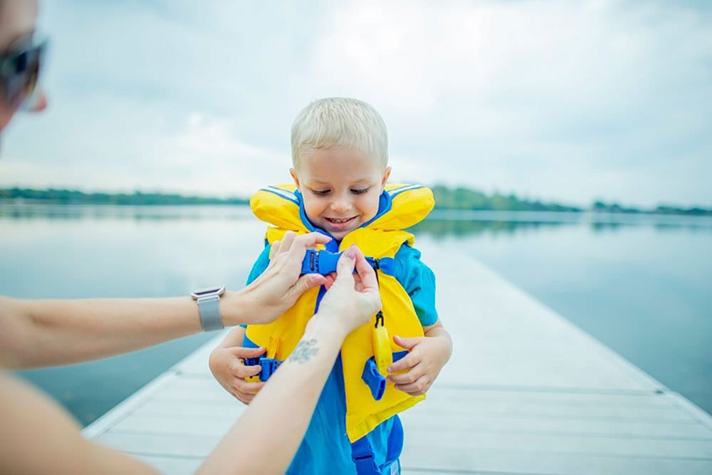 photo of a little boy geeting his life jacket on with the help of an adult