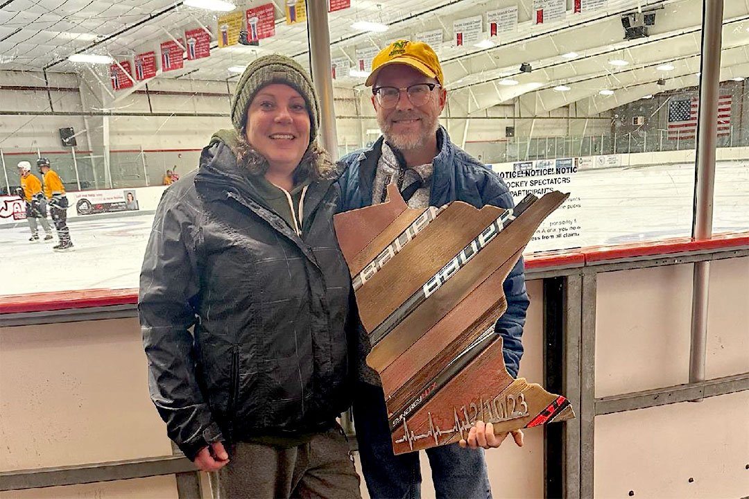 photo of Hubel-Coleman with Rehn and a barn wood and hockey stick Minnesota sign she made for him with a metal heartbeat and date of the event