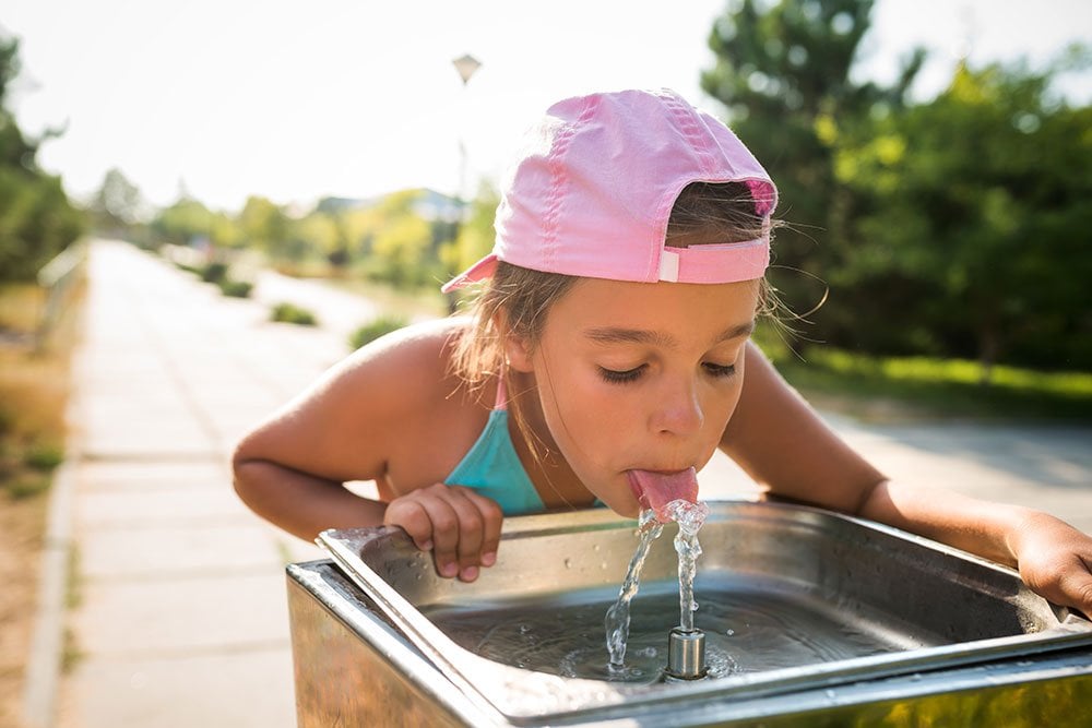 photo of a little girl drinking from the water fountain in the summertime outdoor