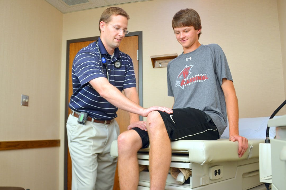 photo of Doctor John Skretvedt performing a sports physical exam on a teenager