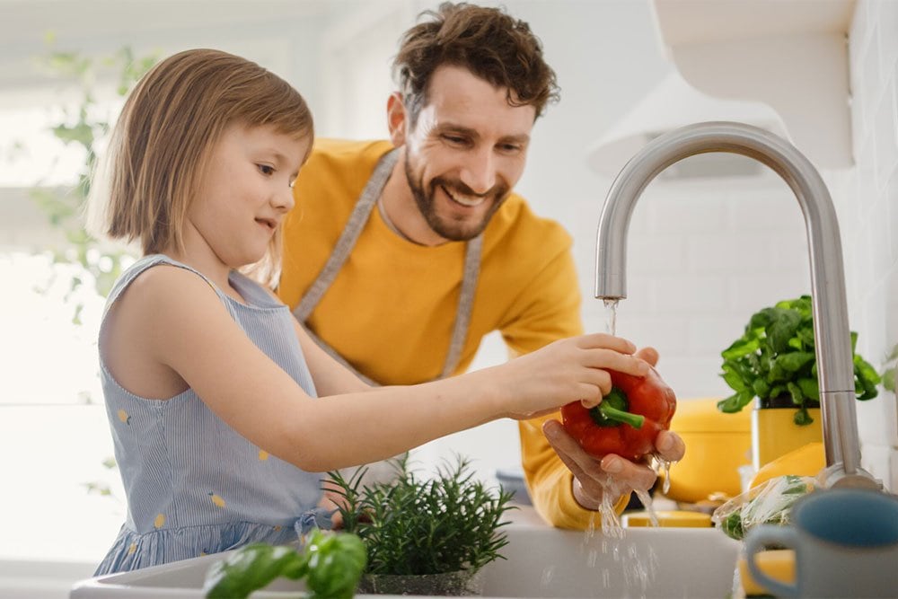 photo of a girl rising a red pepper with her father over the sink