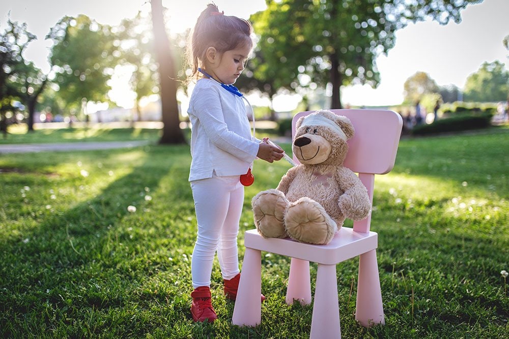 photo of a little girl pretending to give a soft toy bear a shot