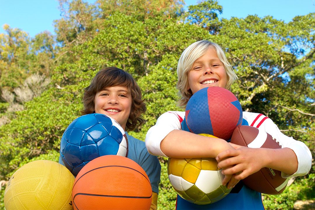 photo of 2 boys holding multiple sports equipment