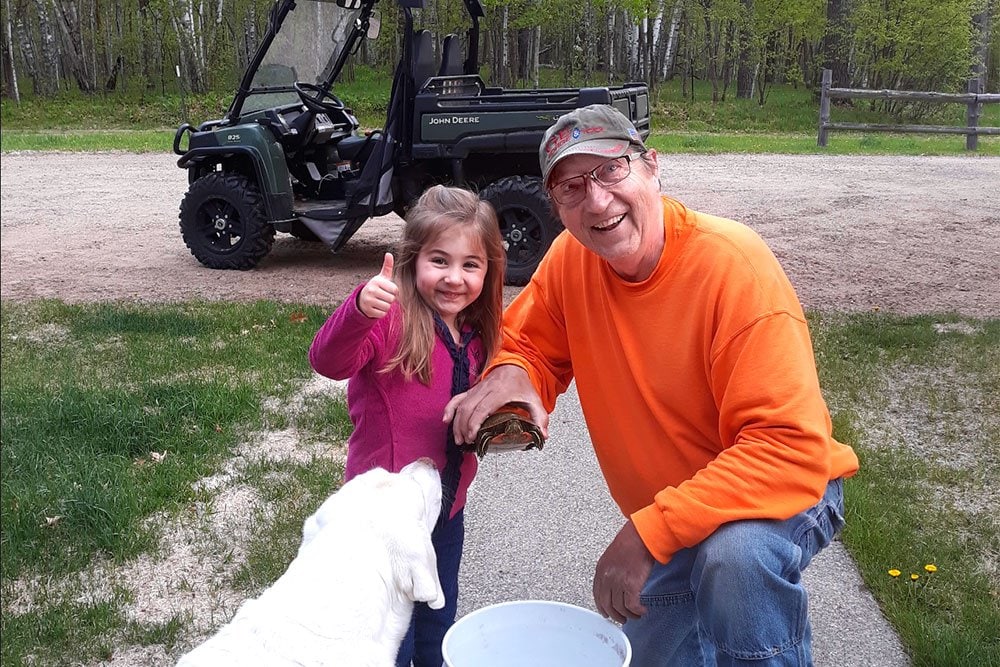 photo of Doug Rach with his gradndaugther and a white dog outdoor