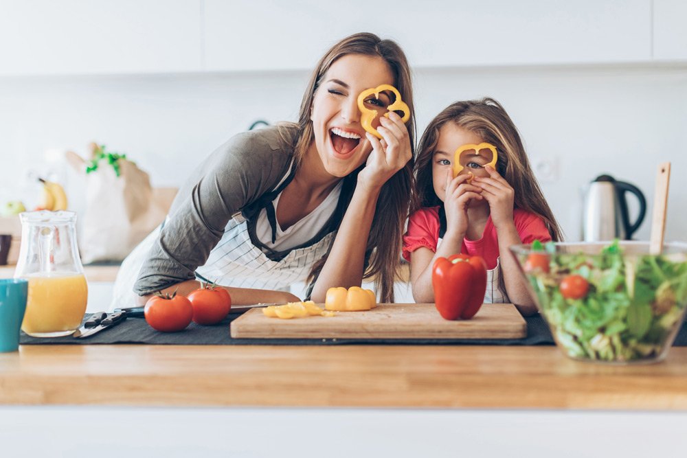 photo of a young woman and a little girl looking through yellow pepper in the kitchen