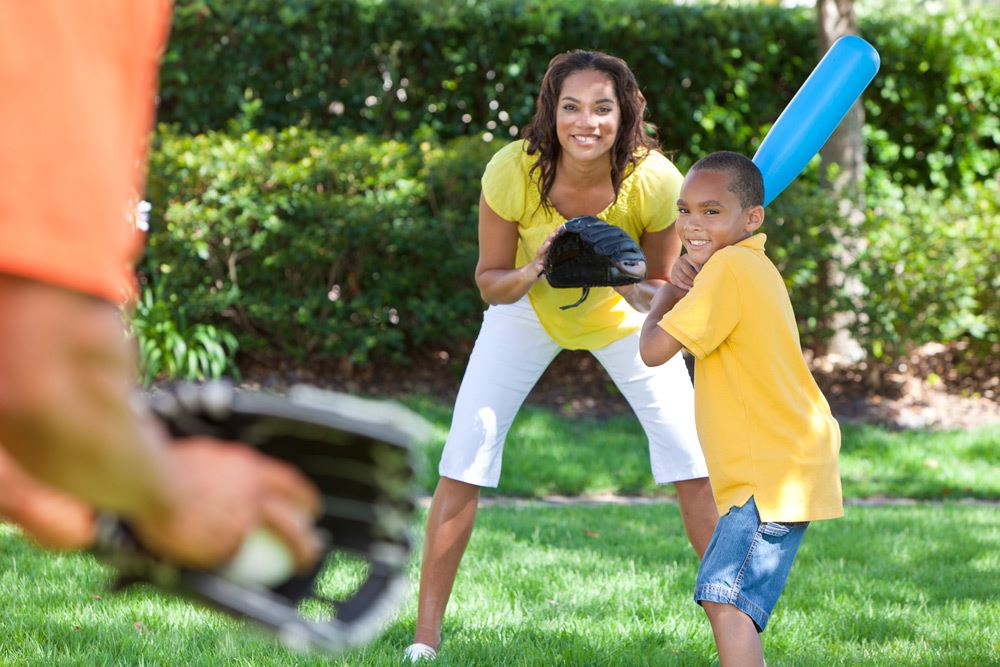 photo of a boy pitching with his mom behind him