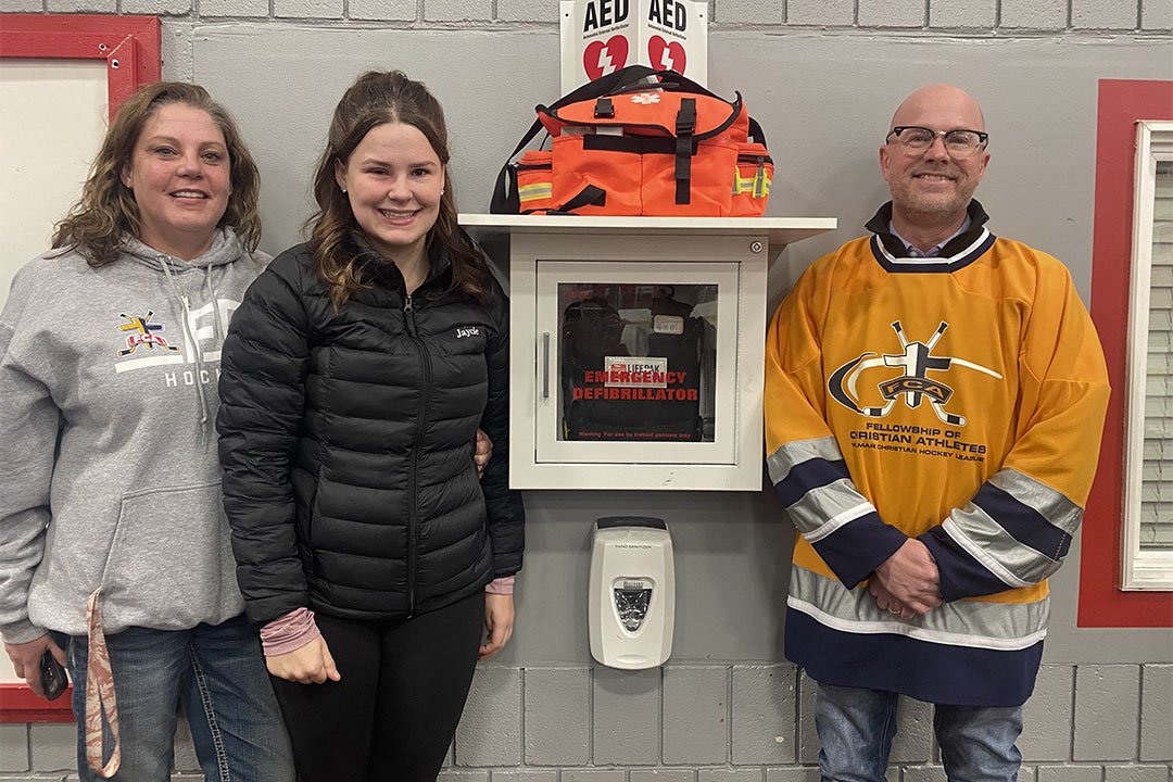 photo of Heather Hubel-Coleman, Jaycie Coleman, and Tim Rehn pose with an AED at the Willmar Civic Center ice rink