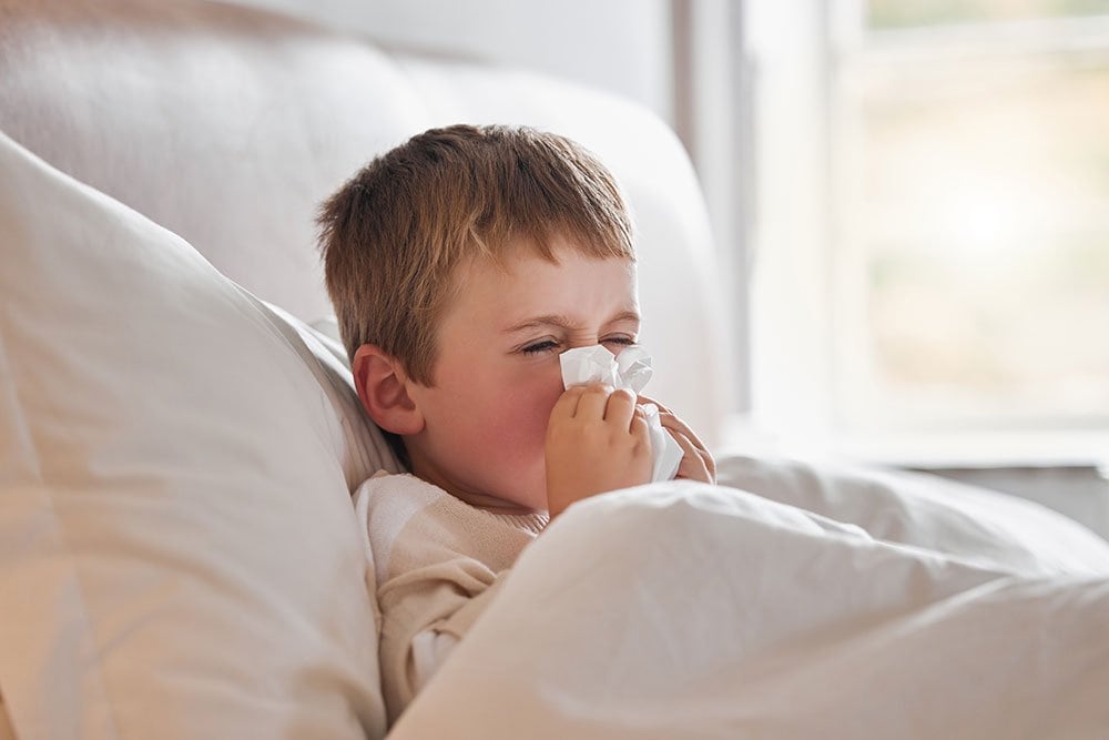 photo of a young boy lied in bed and sneezing