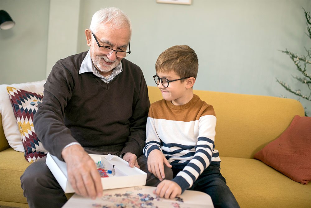 photo of an eldery man starting a puzzle with a young boy