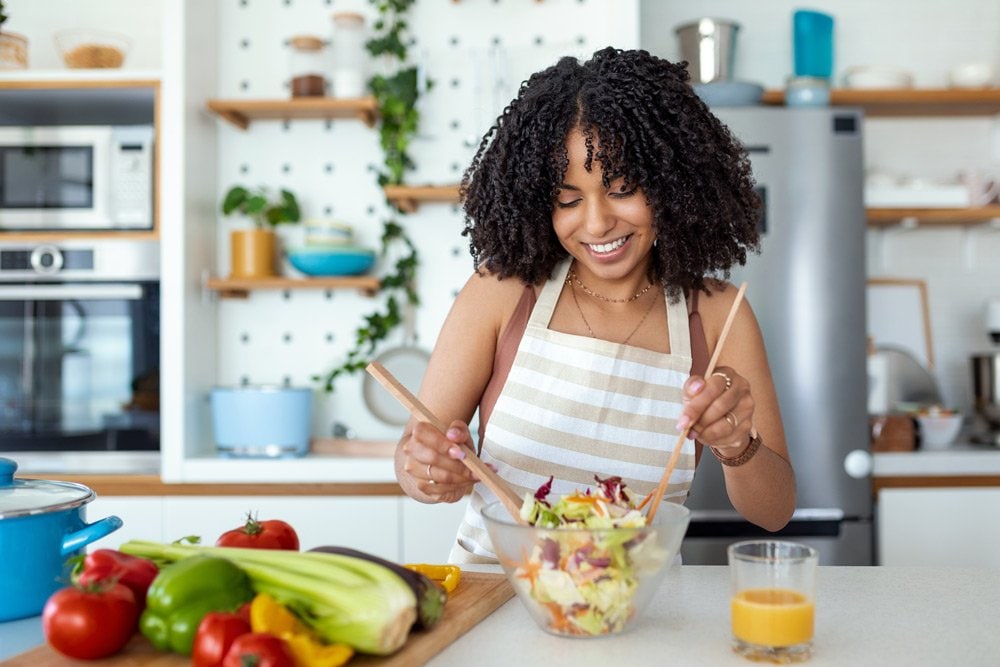 photo of a young woman mixing salad in a kitchen